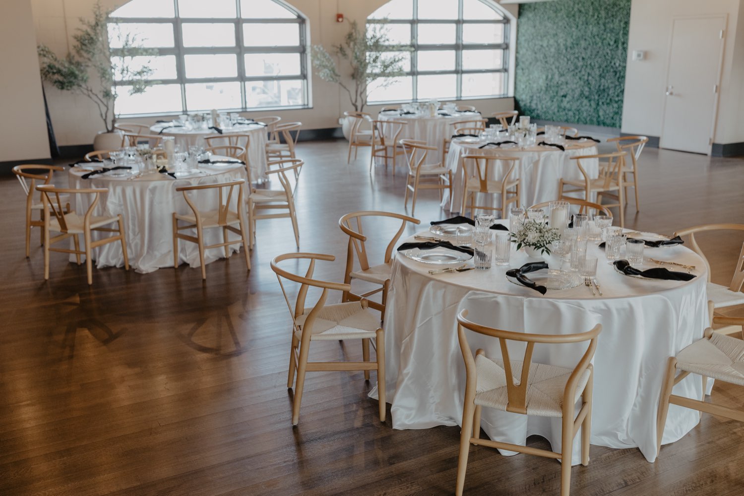 Round tables with black napkins and greenery wall
